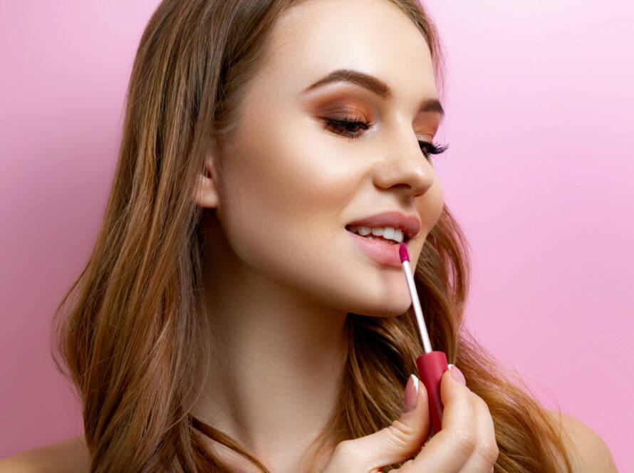 girl-applying-lipstick-pink-background